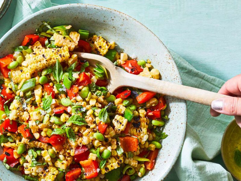 Grilled Corn Succotash in a ceramic bowl with a wooden spoon stirring the mixture