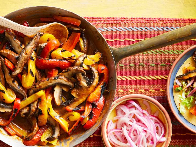 Vegan Barbacoa Fajitas on a red and yellow striped placemat with a bowl of pickled onions