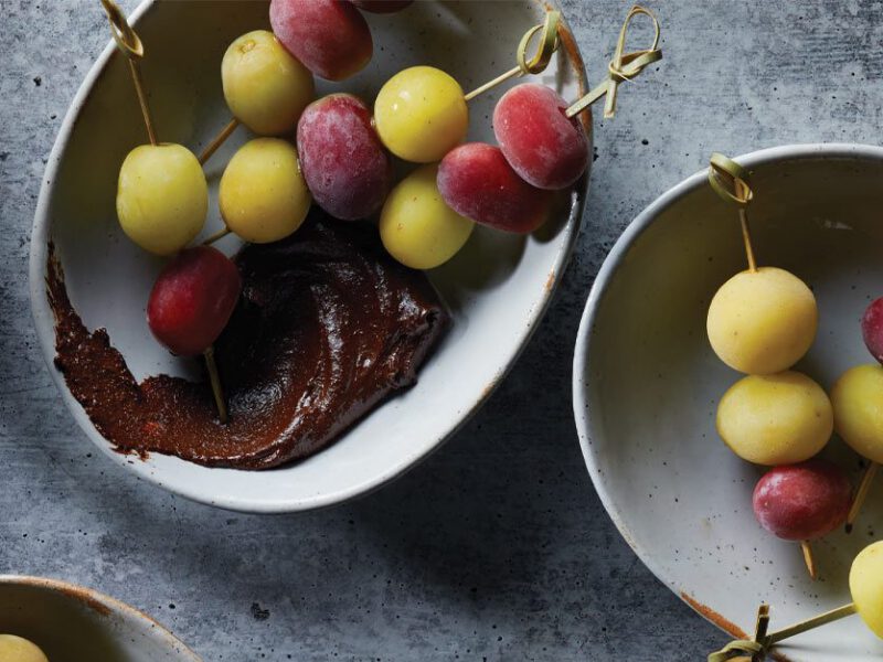 Frozen Grapes with Chocolate Sauce in light gray bowls with a cup of tea on the left
