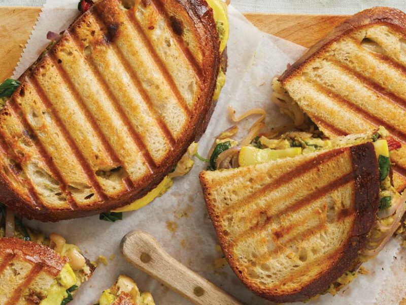 Pesto and Veggie Paninis on parchment paper on a wooden cutting board