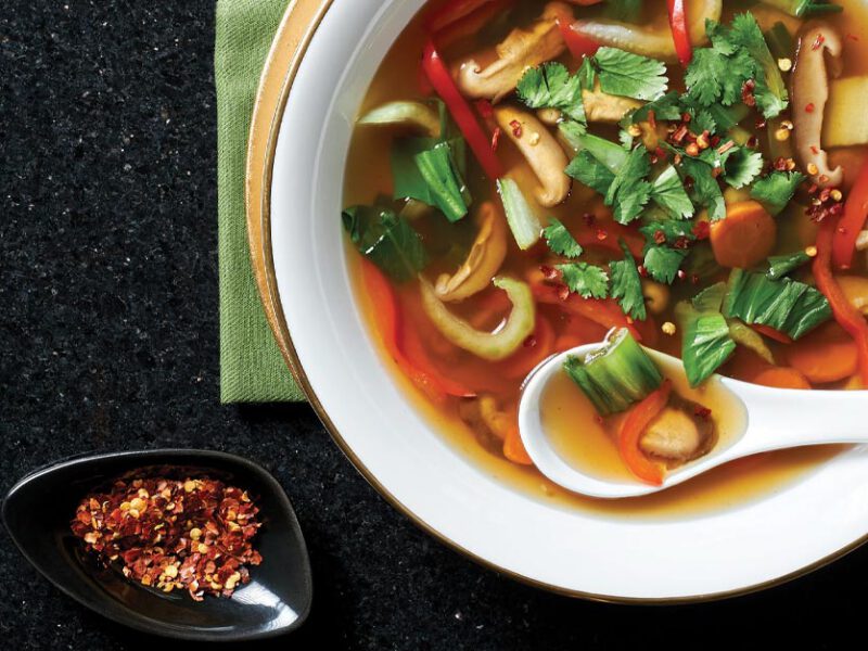 Sweet and Sour Vegetable Soup in a white bowl with a soup spoon on a black granite countertop