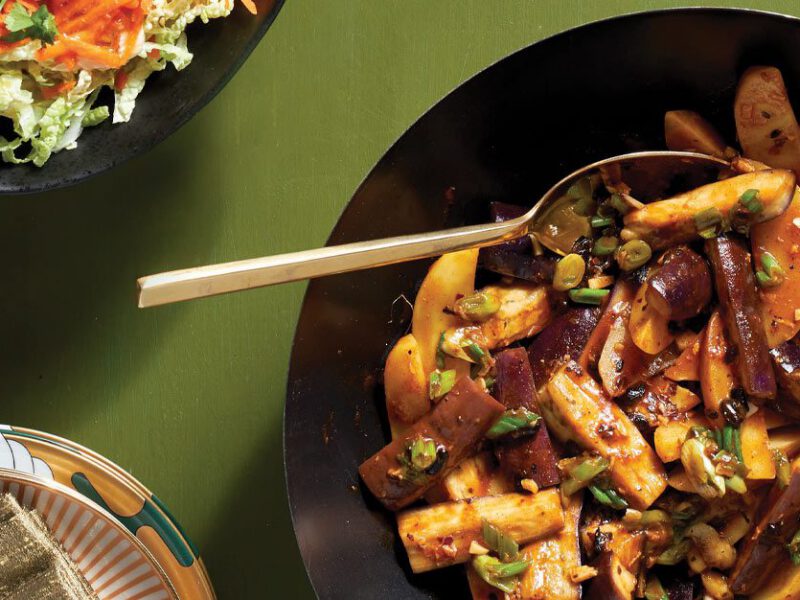 Sichuan Eggplant with Potatoes in a black bowl with a metal spoon against a green background
