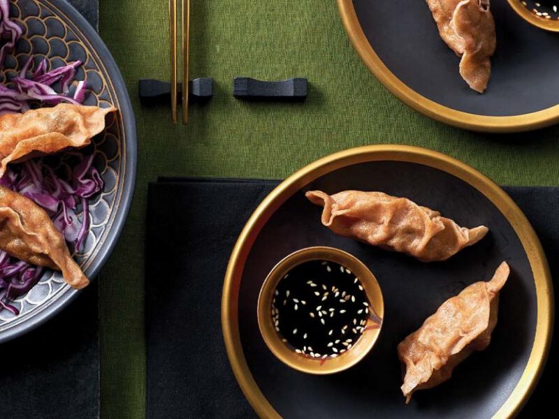 Sweet Potato and Shiitake Mushroom Dumplings on black and gold plates with a small bowl of soy sauce against a green tabletop