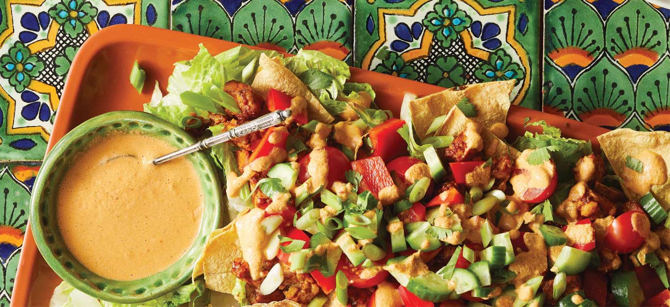 Tempeh Nacho Salad with Creamy Chipotle Dressing on an orange tray sitting on colorful Mexican tiles