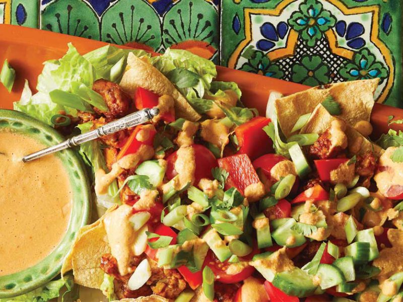 Tempeh Nacho Salad with Creamy Chipotle Dressing on an orange tray sitting on colorful Mexican tiles