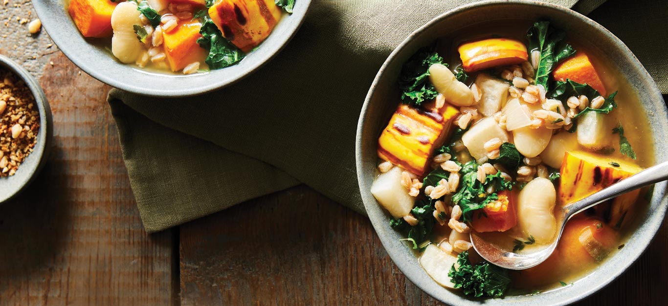 Roasted Garlic, Delicata Squash, and Farro Stew in light gray bowls on a wooden tabletop