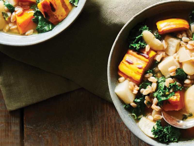 Roasted Garlic, Delicata Squash, and Farro Stew in light gray bowls on a wooden tabletop