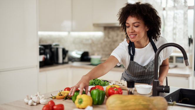 African American woman in an apron reaches across a kitchen counter for bell peppers