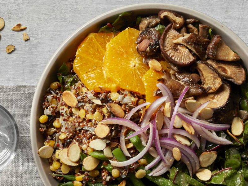 Mixed Grain Bowls with Mushrooms and Lentils on a wooden tabletop with a glass of water to the left