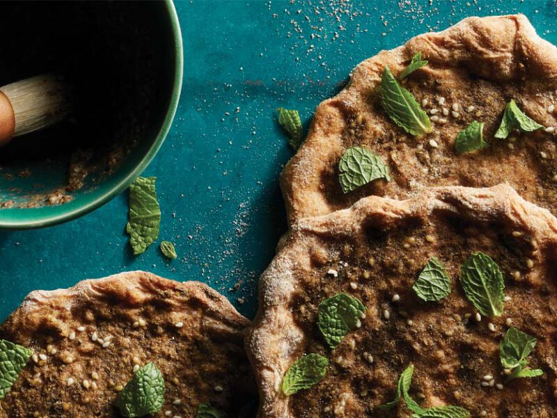 Za’atar-Spiced Flatbreads (Manakeesh) on a blue tabletop next to a bowl za'atar spice
