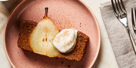 a slice of a gingerbread loaf cake with a sliced pear in the middle, topped with a dollop of vegan whipped cream