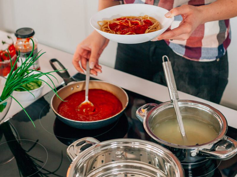 Woman standing over a stove adding pasta cooking water to jarred pasta sauce to make it better