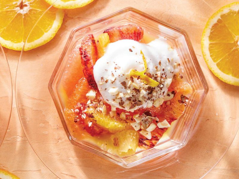 Poached Citrus with Aquafaba Whipped Cream in a cocktail glass on a peach colored background