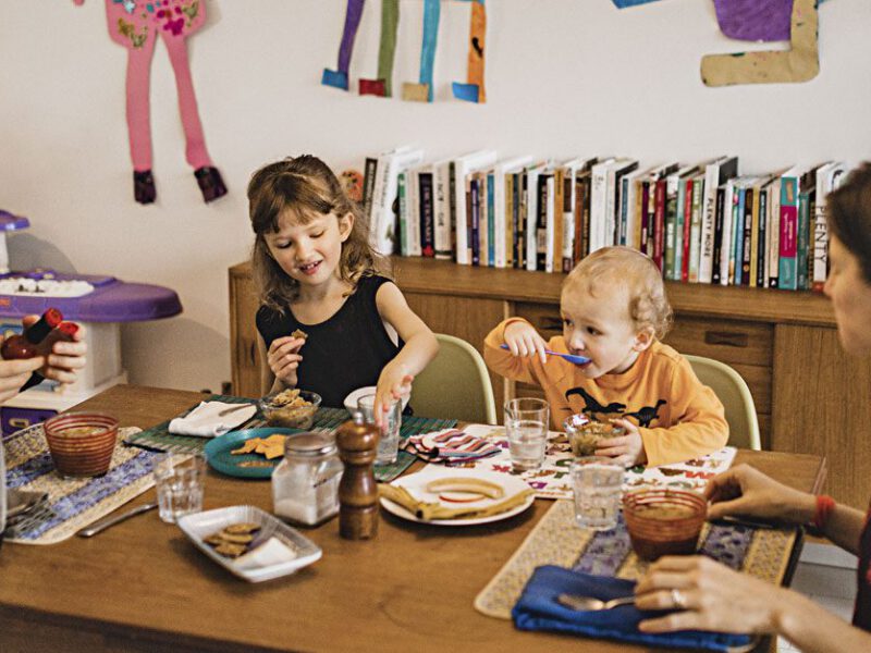 A man and woman sit at opposite ends of a table, with two young children sitting between them, enjoying a plant-based meal as a family