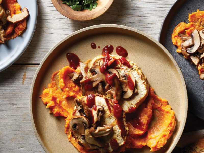 Roasted Celeriac Steaks with Mushrooms and Sweet Potato Mash on a tan plate on a wooden tabletop