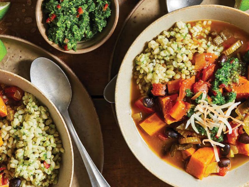 Caribbean Sweet Potato Stew in tan ceramic bowls with a side of green sauce in a small bowl