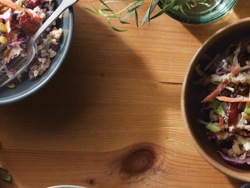 Hearty Winter Slaw with Quinoa and Cranberries in brown and blue bowls against a wood tabletop
