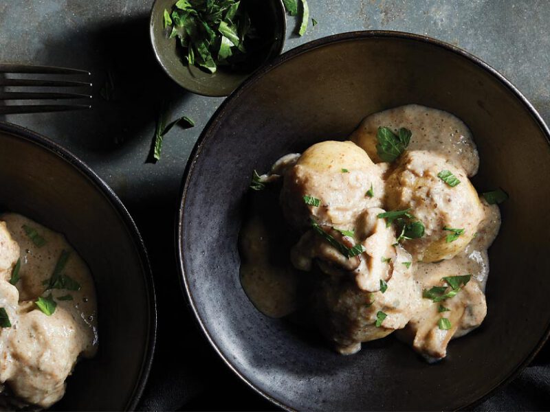 German Potato Dumplings with Mushroom Gravy in black ceramic bowls with a smaller bowl of chopped parsley