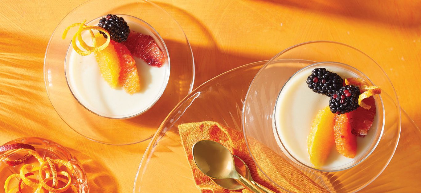 Orange Vegan Panna Cotta with Blackberries in glass dishes against an orange background