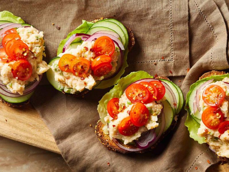 White Bean Toasts with Veggies on a brown cloth napkin resting on a wood cutting board