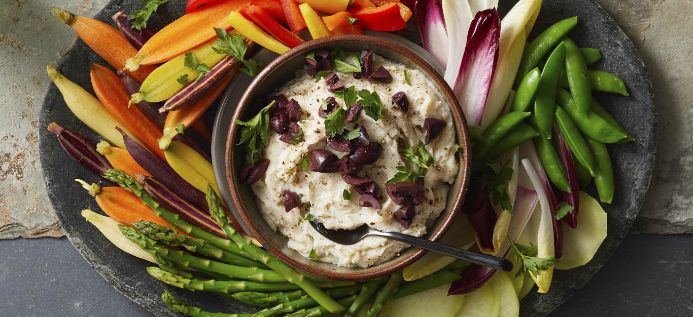 Skordalia (Greek Potato Garlic Dip) in a brown bowl surrounded by fresh veggie slices