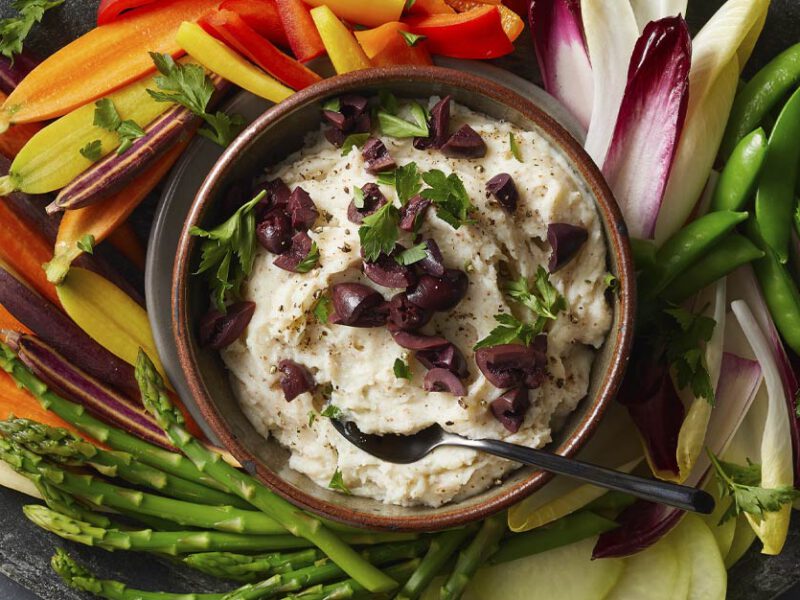 Skordalia (Greek Potato Garlic Dip) in a brown bowl surrounded by fresh veggie slices