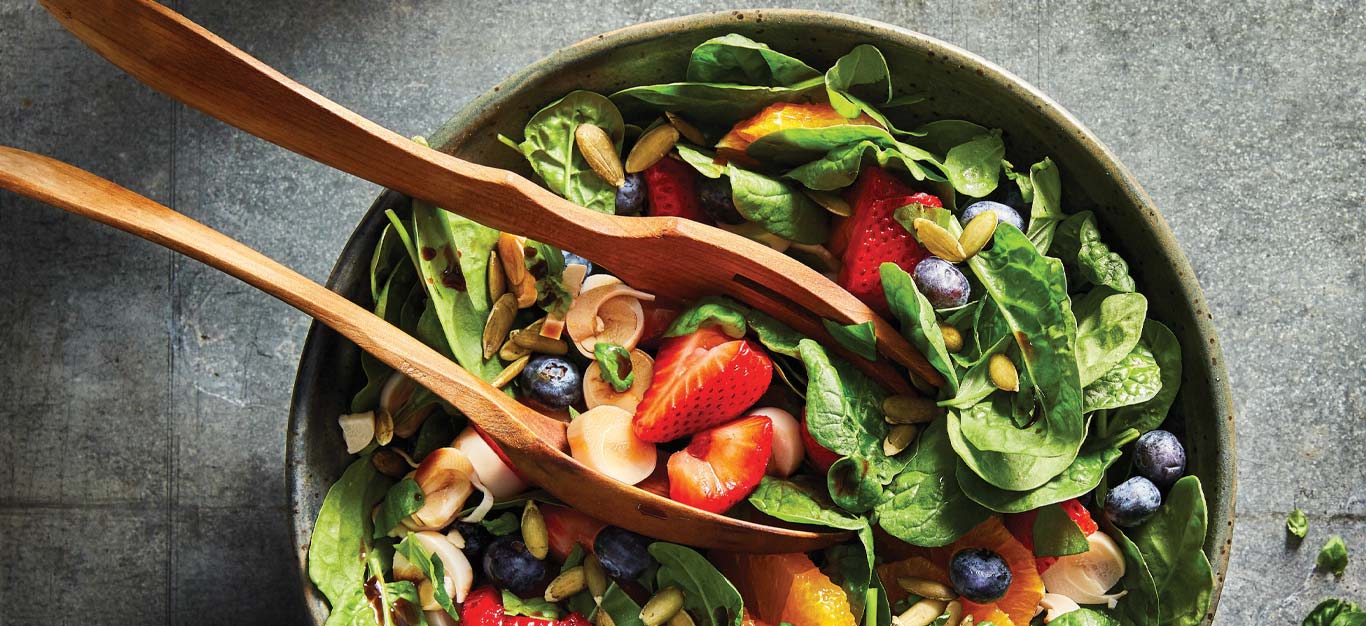 Sweet Spinach and Berry Salad in a green ceramic serving bowl with wooden tongs