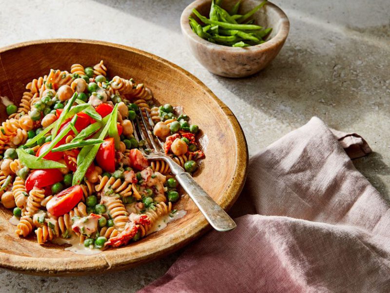 Creamy Chickpea Pasta Primavera in a wooden bowl with a metal fork on a cement countertop