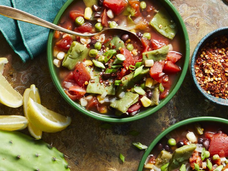 Sopa de Nopales in green bowls surrounded by lemon wedges, cactus paddles, and red pepper flakes