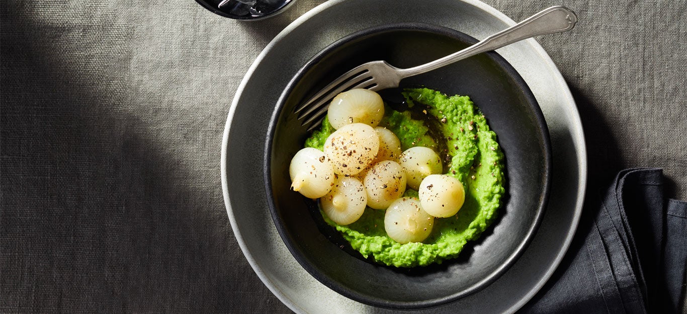 Braised Cipollini Onions with Spring Pea Puree on a dark grey plate