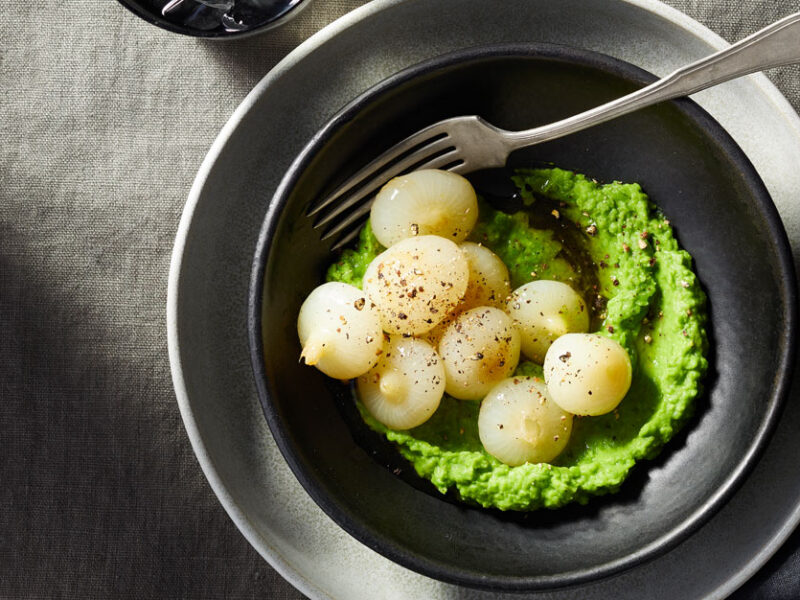 Braised Cipollini Onions with Spring Pea Puree on a dark grey plate