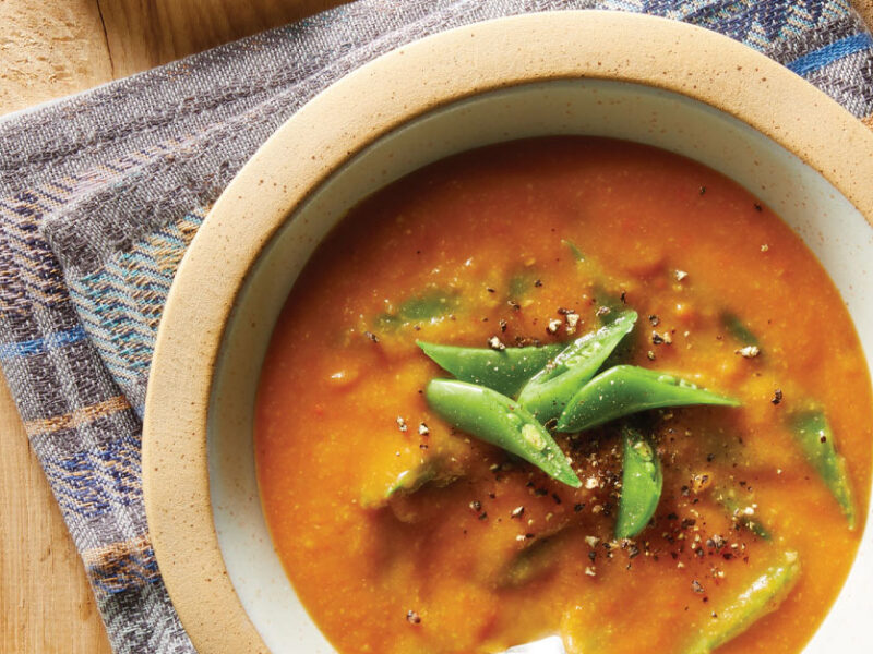 Creamy Carrot and Pea Soup in a white and tan bowl on a blue cloth napkin