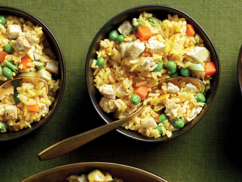 Oil-Free Tofu Fried Rice in small black bowl with metal spoons against a green tablecloth
