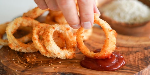 A hand dips an oil-free fried onion ring—from Kiki Nelson's Plantifully Lean cookbook—in ketchup