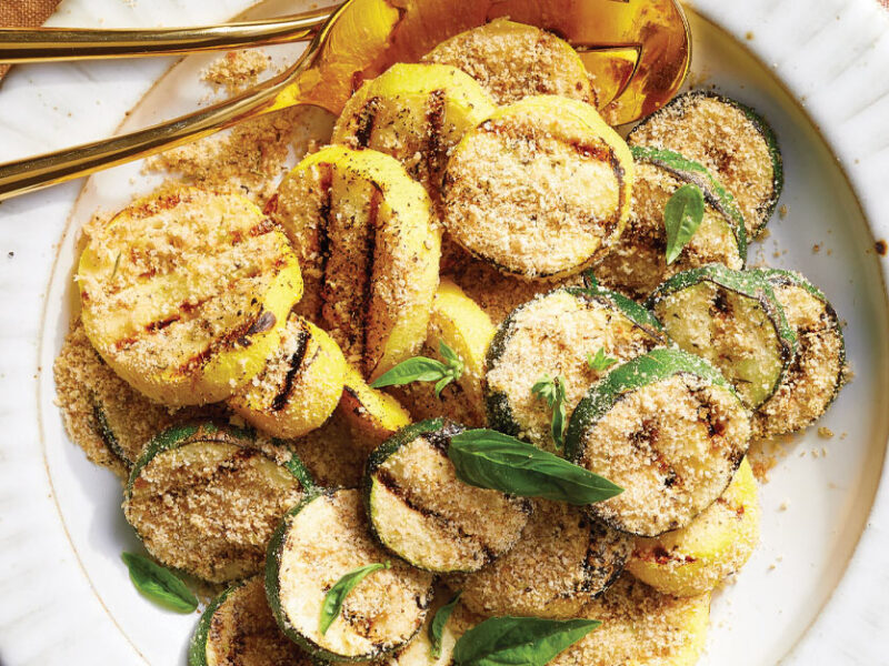 Grilled Summer Squash with Seasoned Bread Crumbs on a white plate with gold metal serving spoons