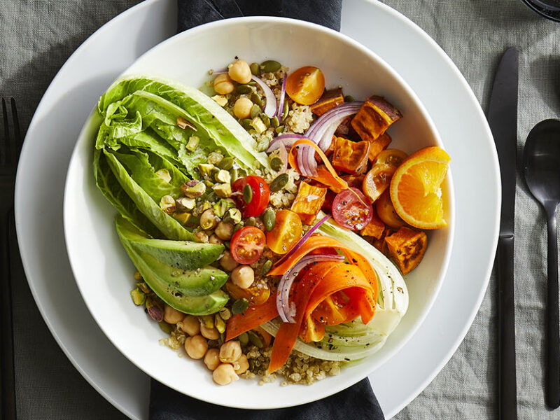 Bowl in a restaurant place setting, in the bowl is an array of whole food plant-based ingredients including chickpeas, pumpkin seeds, and tofu, layered over a heart of romaine lettuce