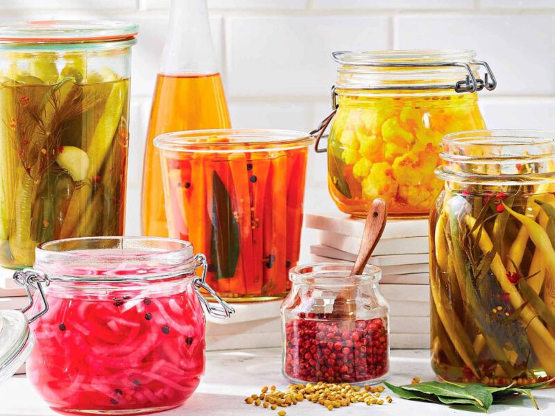 An array of different low-sodium quick-pickled vegetables, including pickles, carrots, quick-pickled red onions, and more, with a cruet full of vinegar in the background