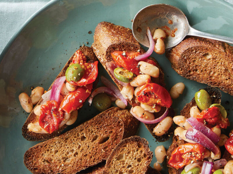 Roasted Tomato, White Bean, and Olive Bruschetta on a light blue ceramic plate