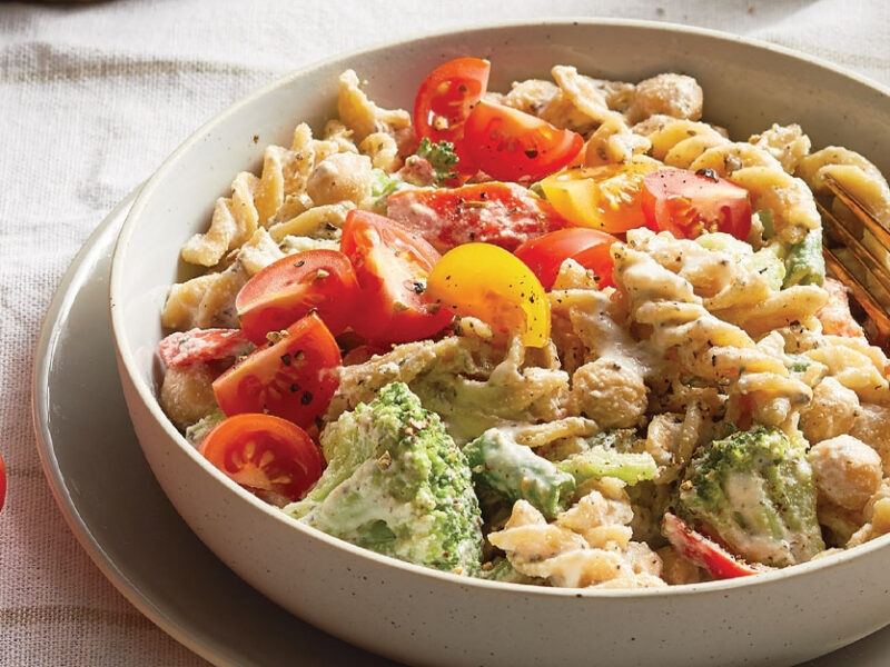 Healthy Creamy Pasta with Veggies and Chickpeas in a white ceramic bowl with gold metal fork