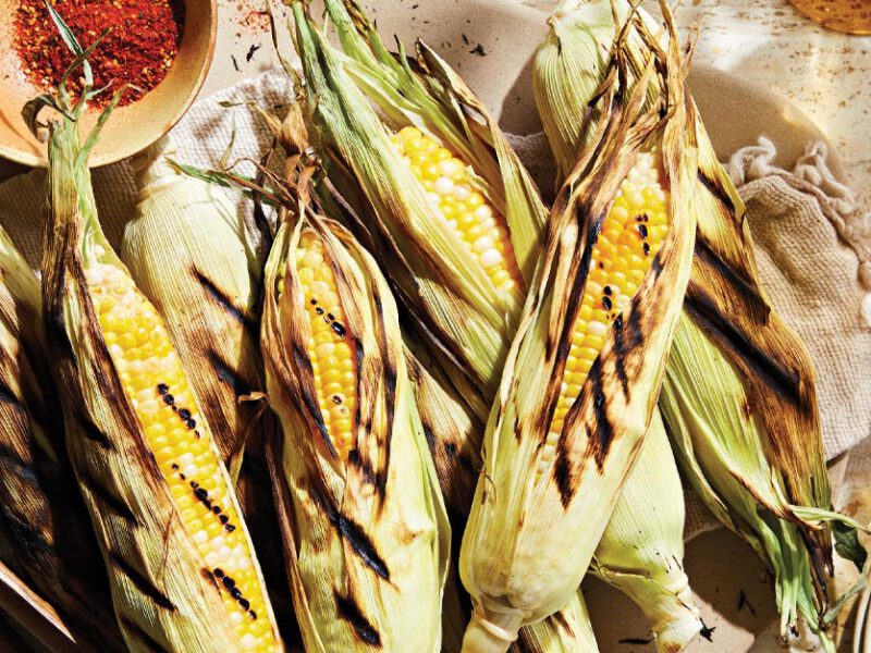Perfectly Tender Corn on the Cob on a beige kitchen towel with a bowl of red seasoning