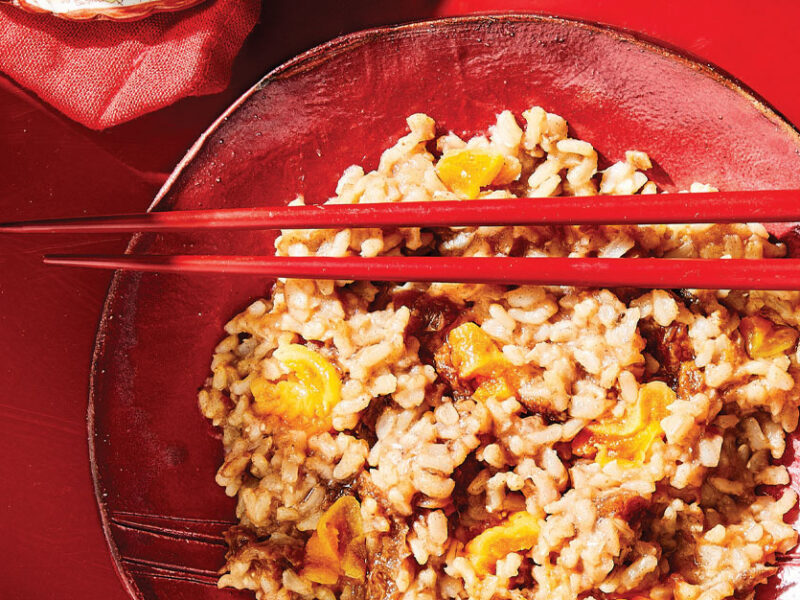 Sweet Congee with Dates and Apricots in a red bowl with red chopsticks against a red background