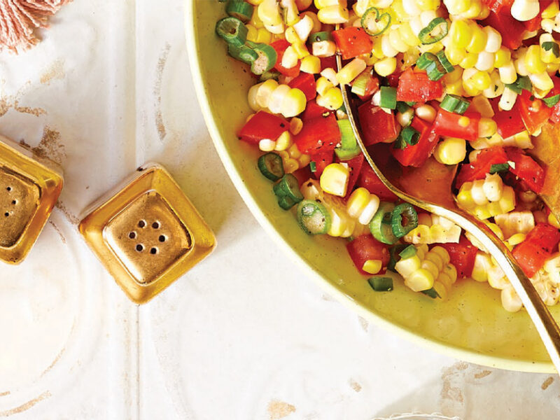 Spicy Corn and Tomato Salad in a yellow serving bowl with metal serving utensils