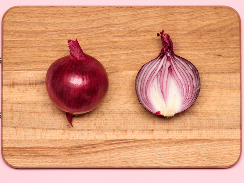 two halves of a red onion lying on a cutting board, with one half facing cut side down and the other half facing cut side up, on a solid pink abstract background