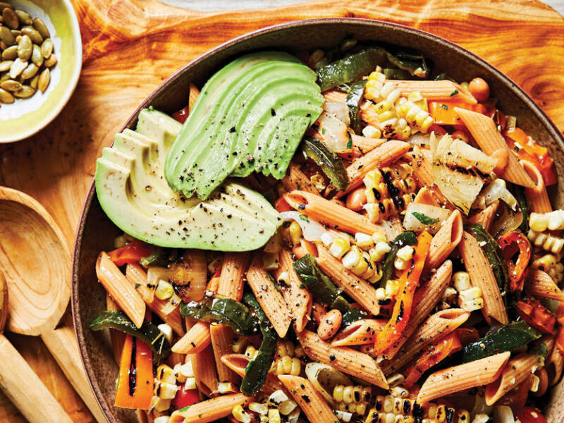 Fajita Pasta Salad in a gray bowl on a wood cutting board with a small bowl of pepitas