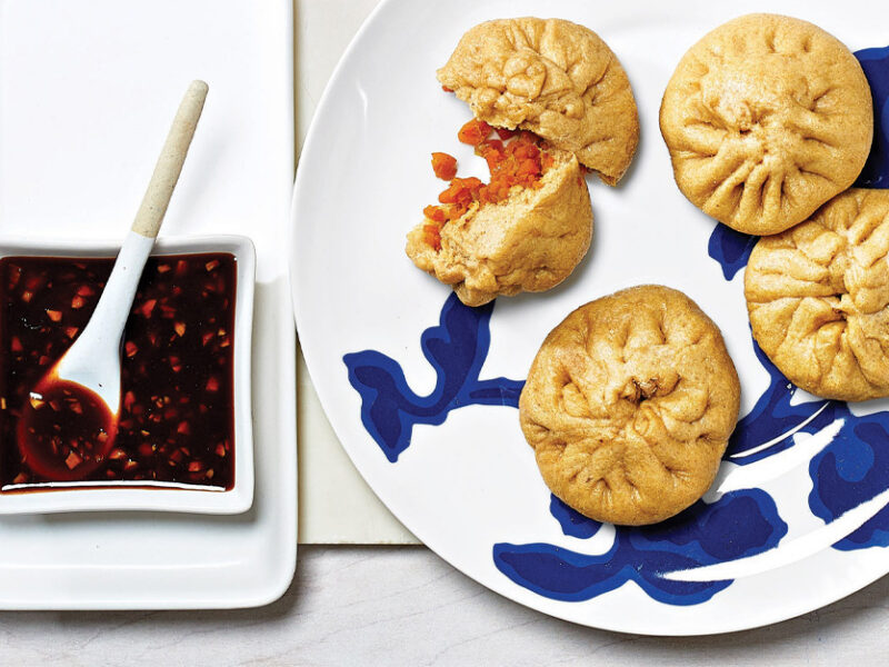 Hannah Che’s Vegan Bao Buns on a blue and white china plate next to a square dish of spicy soy dipping sauce
