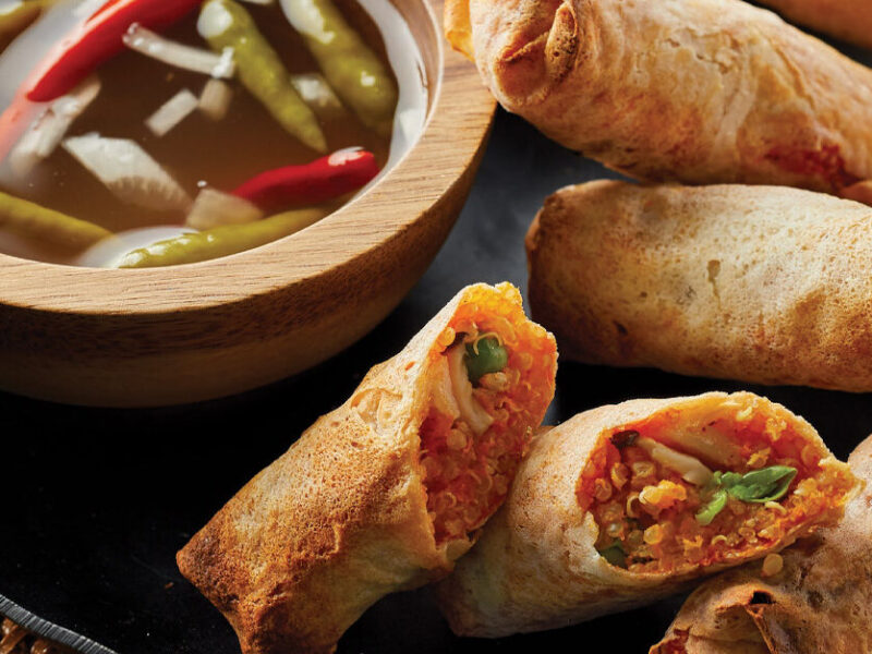 Air-Fried Vegan Lumpia on a black plate with a bowl of dipping sauce