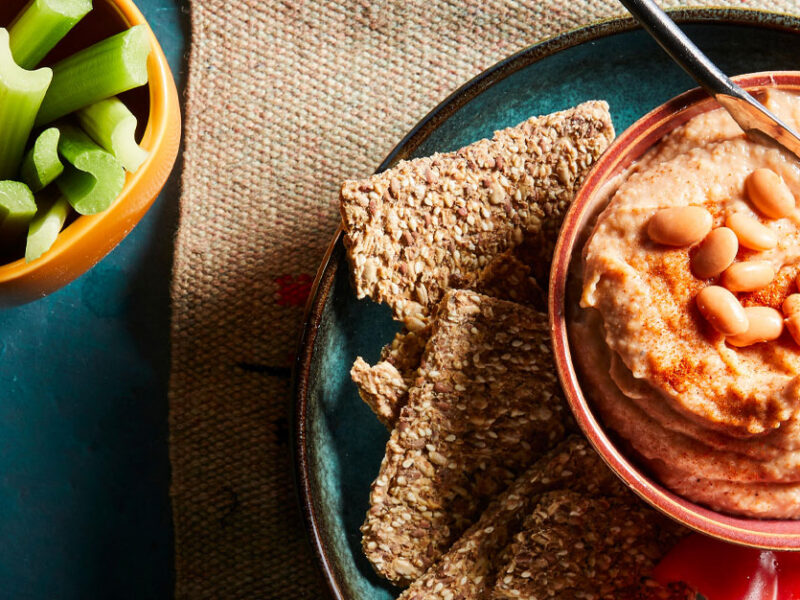 Pinto Bean Spread in a small orange bowl on a plate with crackers and celery sticks