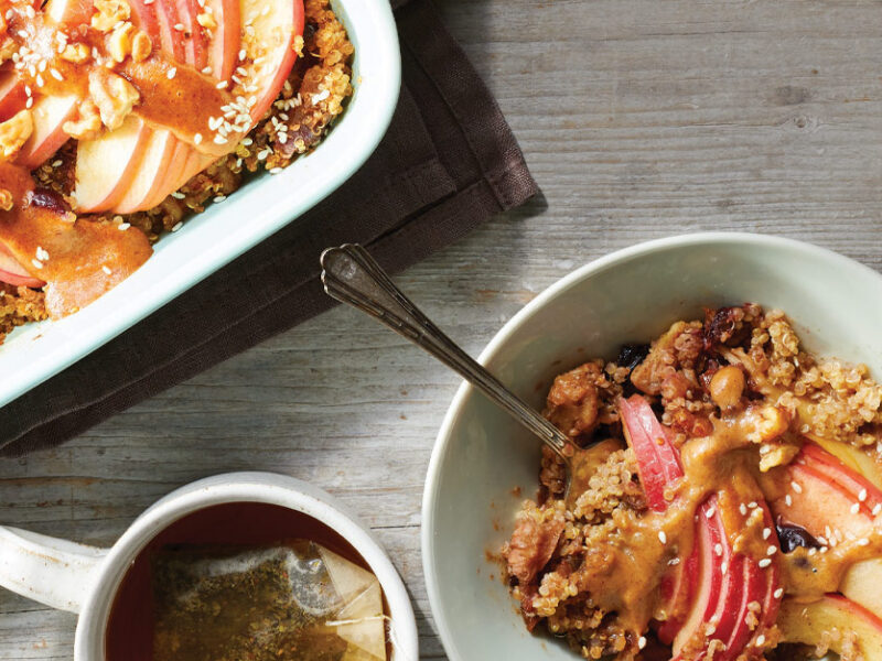 Quinoa and Apple Breakfast Casserole with Cherry Drizzle in a white bowl next to a white casserole dish