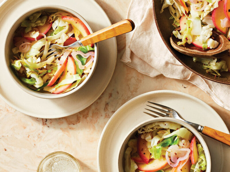 Tangy Cabbage and Apple Sauté in small white bowls with forks against a beige marble countertop