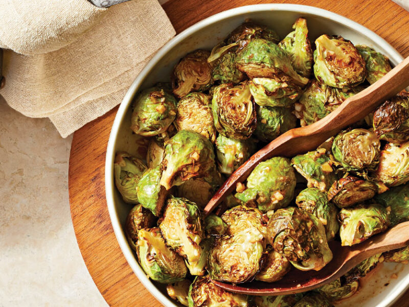 Sweet and Spicy Air-Fried Brussels Sprouts in a white bowl with wooden serving spoons